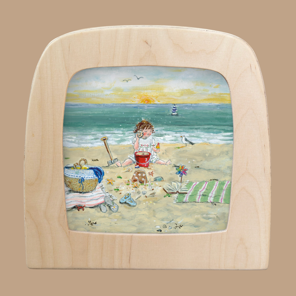 A child plays with a red bucket on a sandy beach, surrounded by seashells, a towel, and a basket. A sailboat and sunset complete the scene—perfect for home decor with the "Silhouette Only - I Hear the Sea for Toverlux Lamp.