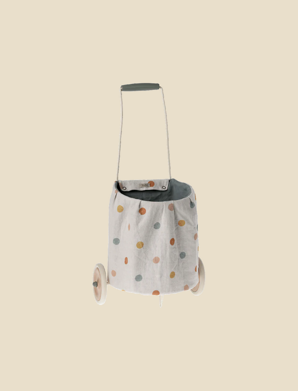The Maileg Trolley, Multi dots - Blue is a small wheeled trolley with a washable linen bag in colorful polka dots, gray interior, and gray handle, shown against a plain beige background.