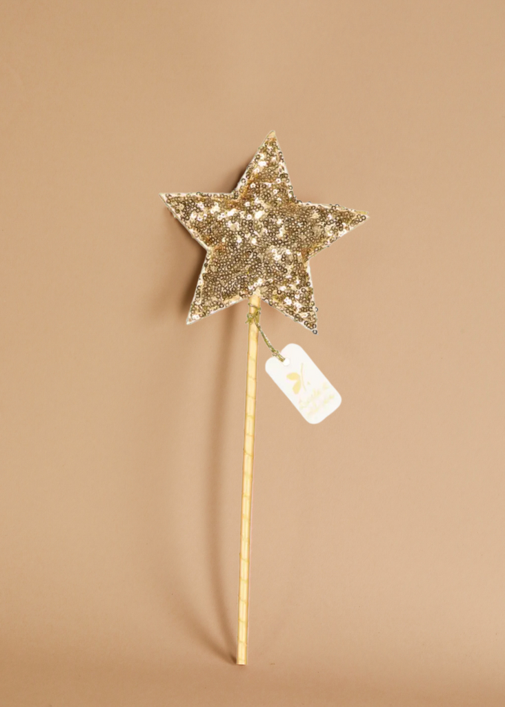 The Magic Wand - Gold Sequin Star features a sparkling gold sequin star, a wooden handle, and a small white tag, shown against a plain beige background.