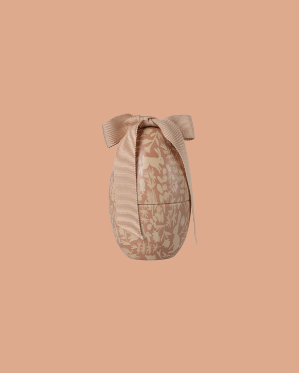 The Maileg Easter Egg, Small - Powder features a cream floral pattern and a textured bow on top, presented against a solid peach background.