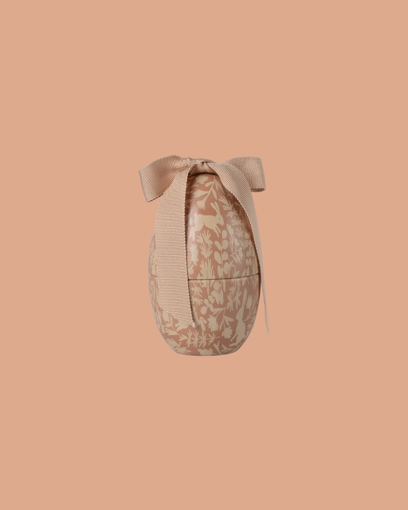 The Maileg Easter Egg, Small - Powder features a cream floral pattern and a textured bow on top, presented against a solid peach background.