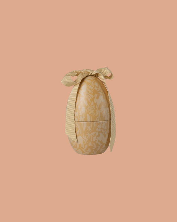 The Maileg Easter Egg, Small - Cream Yellow features a subtle floral pattern and a textured yellow ribbon at the top, shown against a solid peach background. Expected arrival: 02/15/26.