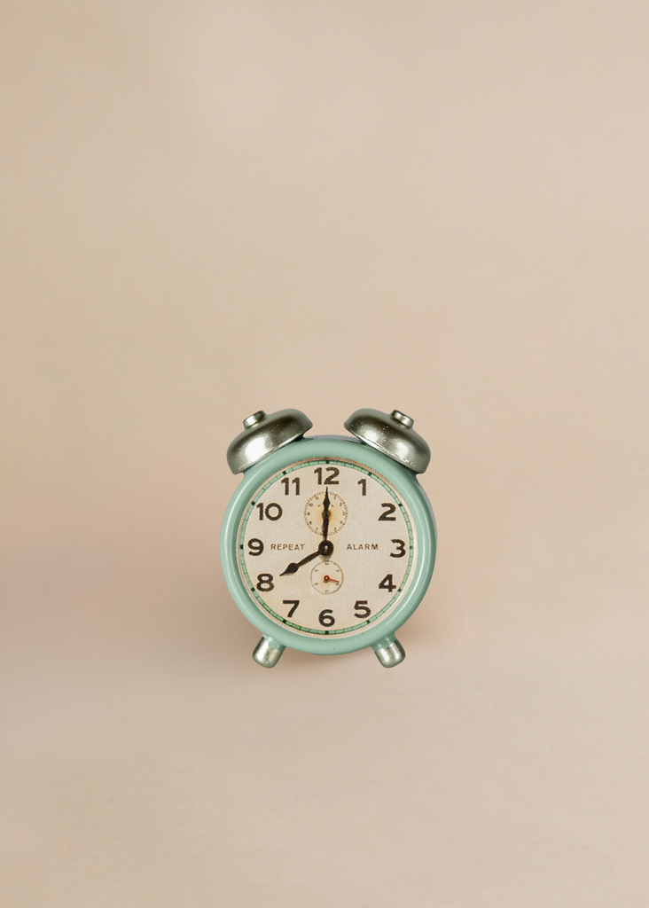 A small, mint green vintage alarm clock sits on a light beige background next to the Maileg Little Sister Bedroom Set. The clock displays 7:00.