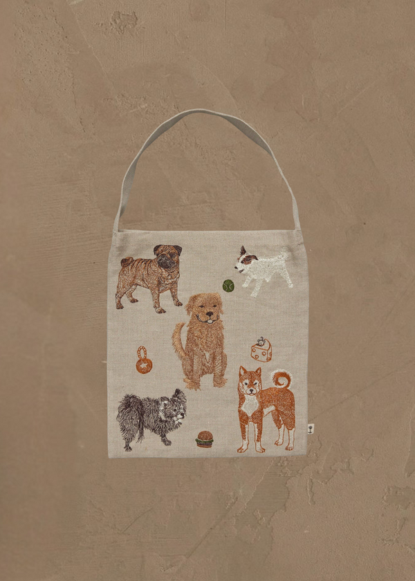The Coral & Tusk Dogs and Toys Tote is a beige bag with embroidered images of six dog breeds and playful dog-themed items, all set on a plain brown textured background.
