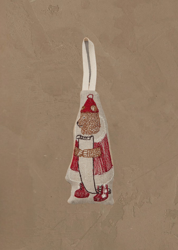 The Coral & Tusk North Pole Bear Ornament features a bear dressed as Santa holding a scroll, complete with a hanging loop—perfect for bringing festive North Pole charm to your Christmas tree. Displayed on a textured tan background.