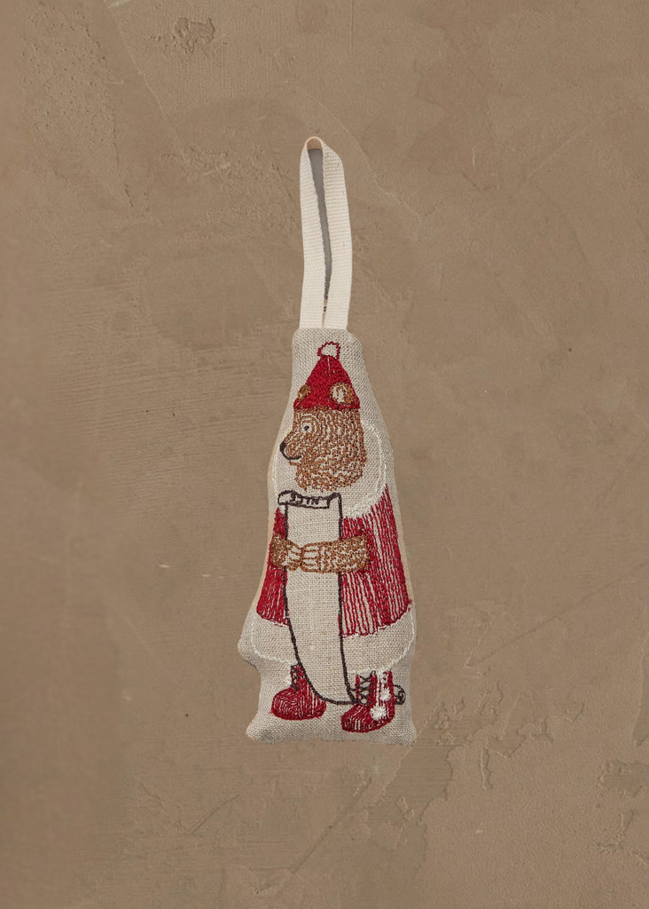 The Coral & Tusk North Pole Bear Ornament features a bear dressed as Santa holding a scroll, complete with a hanging loop—perfect for bringing festive North Pole charm to your Christmas tree. Displayed on a textured tan background.