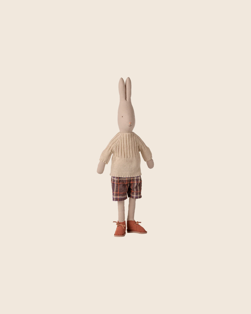 The PRE-ORDER: Maileg Rabbit, Size 4 - Classic - Pants and Knitted Sweater stands upright in plaid pants and a cream sweater, crafted from natural fabrics, against a plain light beige background. Estimated arrival early November.