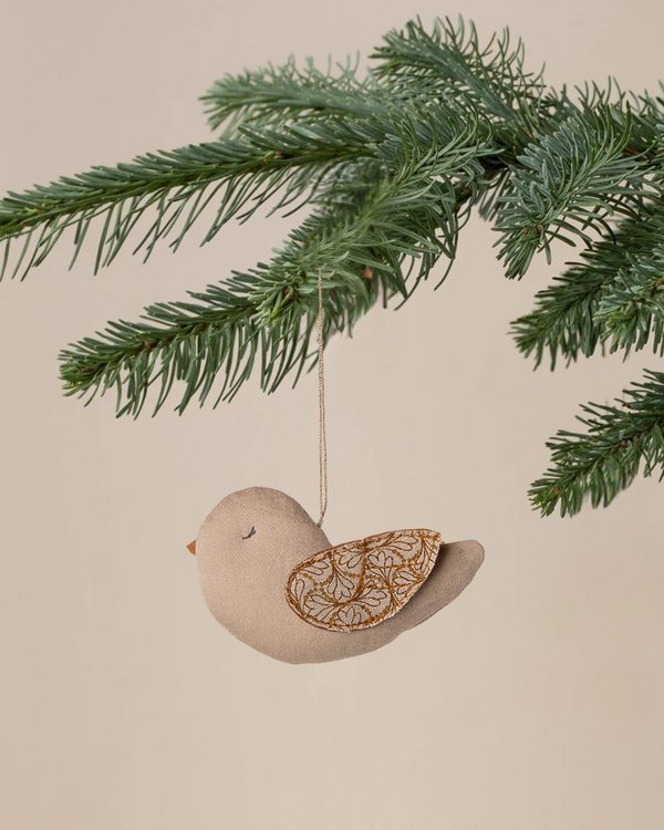 The Maileg Fabric Ornament, Bird - Winter Heart - Sand features decorative wings and hangs from a green pine branch against a beige background, adding charm to your Christmas ornament collection.