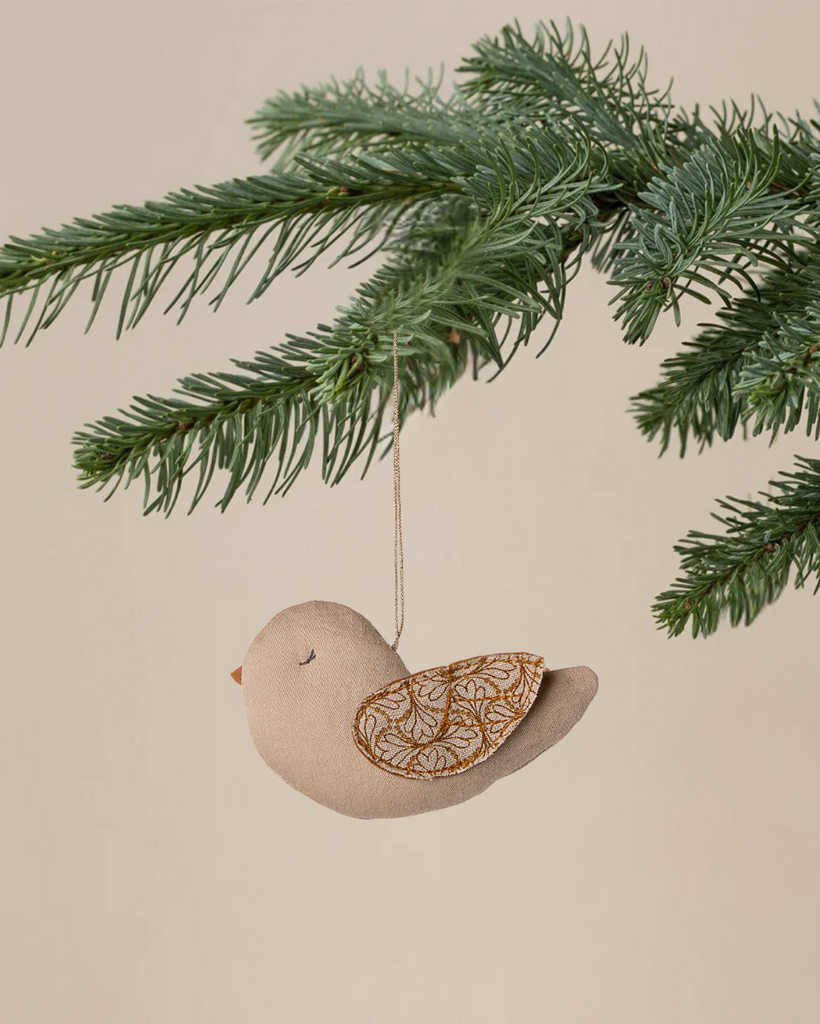 The Maileg Fabric Ornament, Bird - Winter Heart - Sand features decorative wings and hangs from a green pine branch against a beige background, adding charm to your Christmas ornament collection.