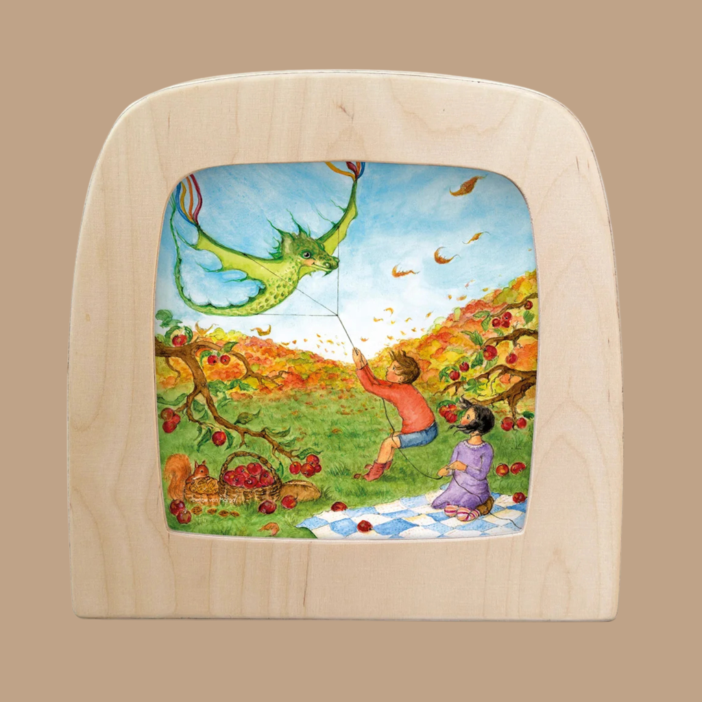 Two children sit on a picnic blanket in an autumn orchard, surrounded by apples hanging from tree branches and colorful leaves swirling in the breeze. One child flies a green dragon-shaped kite, adding a whimsical touch that reflects the enchanting spirit of the “Taming the Dragon” Silhouette for Toverlux Lamp. This silhouette-only design offers a distinctive way to bring warmth and wonder into your home decor.
