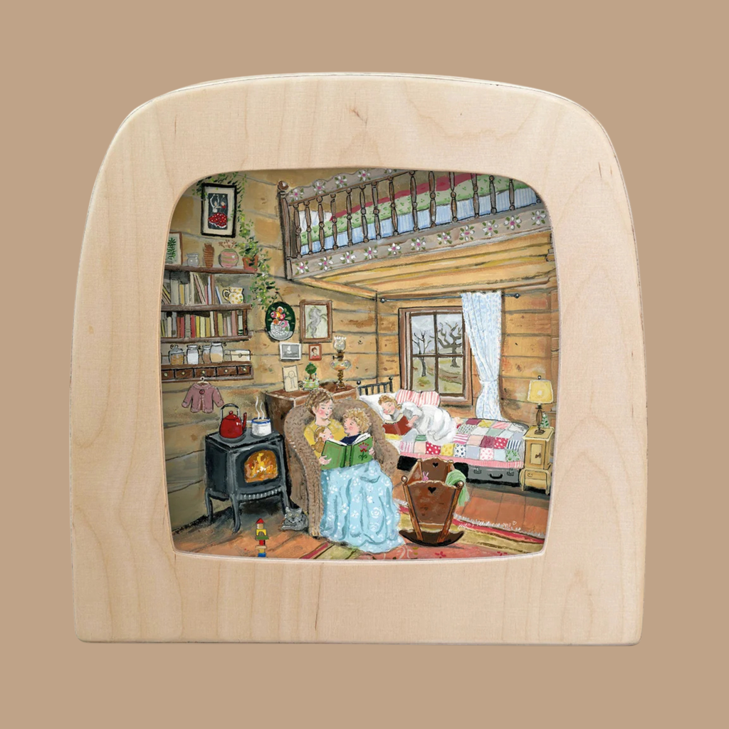 A cozy wooden cabin scene depicts a woman reading to a child by a glowing fireplace, surrounded by a bed, rocking chair, bookshelf, and framed photos. The “Silhouette Only - Story Snuggles Silhouette for Toverlux Lamp” adds an enchanting touch to the space as a unique home decor accent, beautifully showcased in light wood.