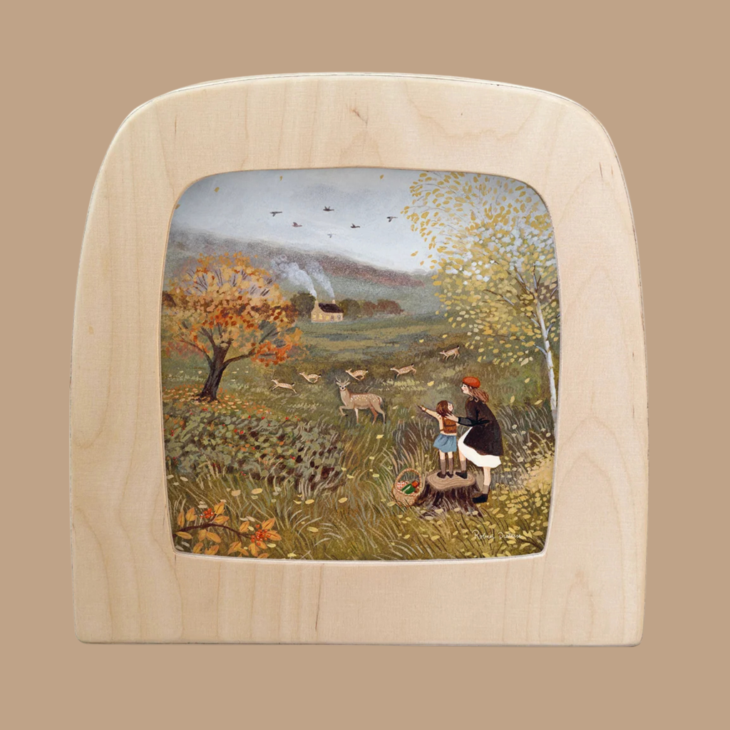 A wooden frame displaying the “Silhouette Only - Fallow Silhouette for Toverlux Lamp” showcases a captivating scene of two people and a dog in a grassy field with deer, autumn trees, and a distant house emitting chimney smoke beneath a cloudy sky—this unique piece from Toverlux perfectly embodies Magic Silhouettes and makes for truly distinctive home decor.