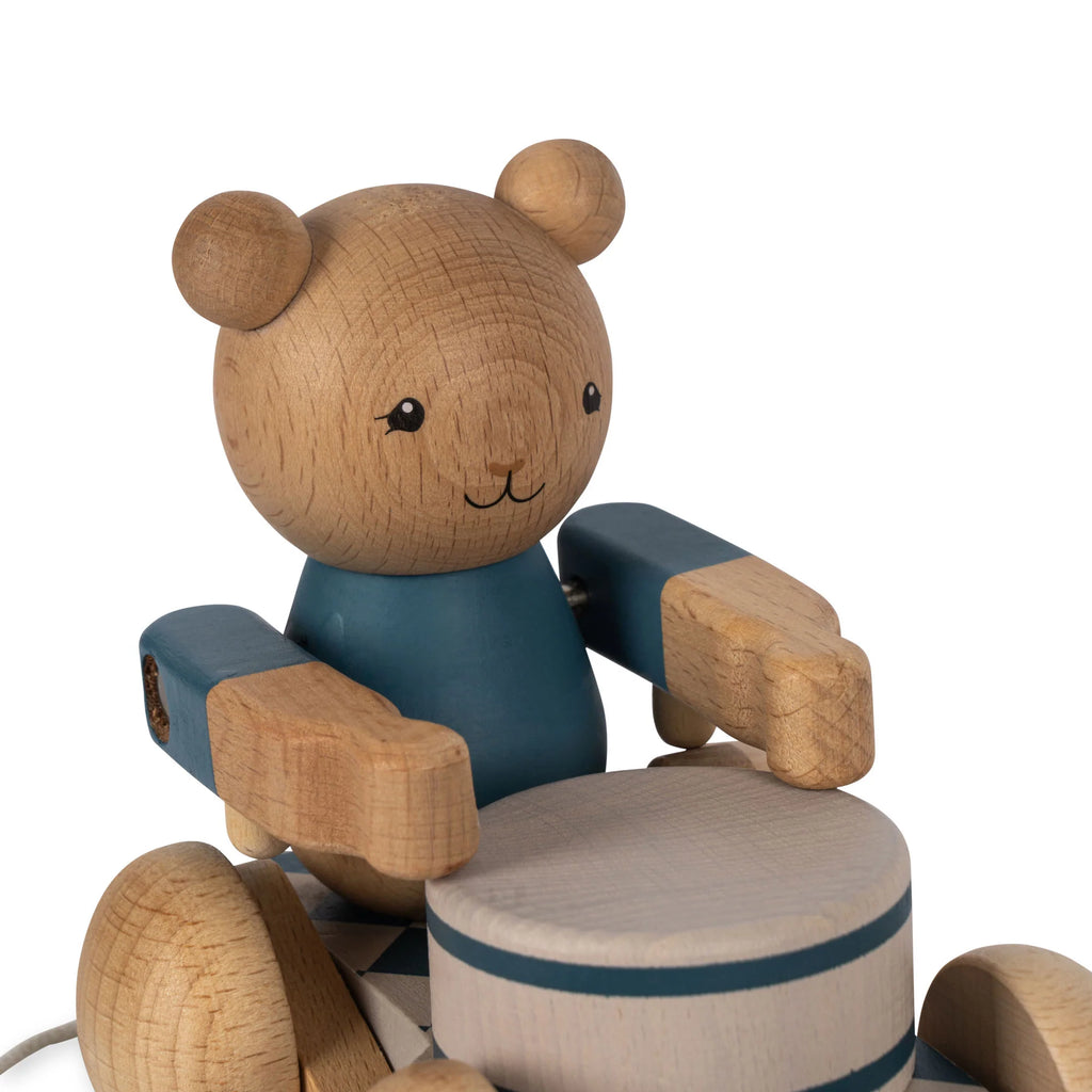 A wooden pull toy bear with articulated limbs painted blue and natural wood, sitting on a wheeled platform, isolated on a white background.