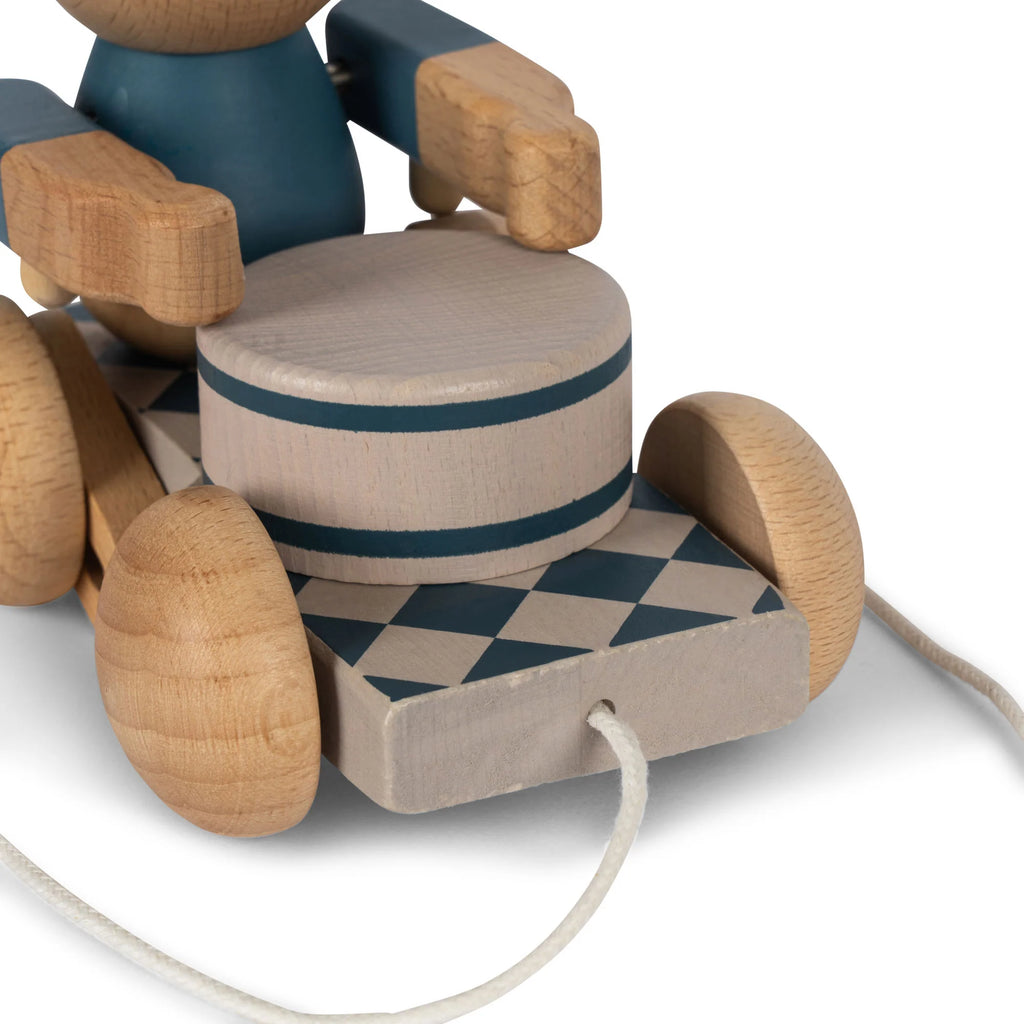 Close-up of a Wooden Pull Toy - Drummer Bear, with cylindrical body parts and wheels, crafted from FSC-certified wood and painted in shades of blue and natural wood, featuring geometric patterns.