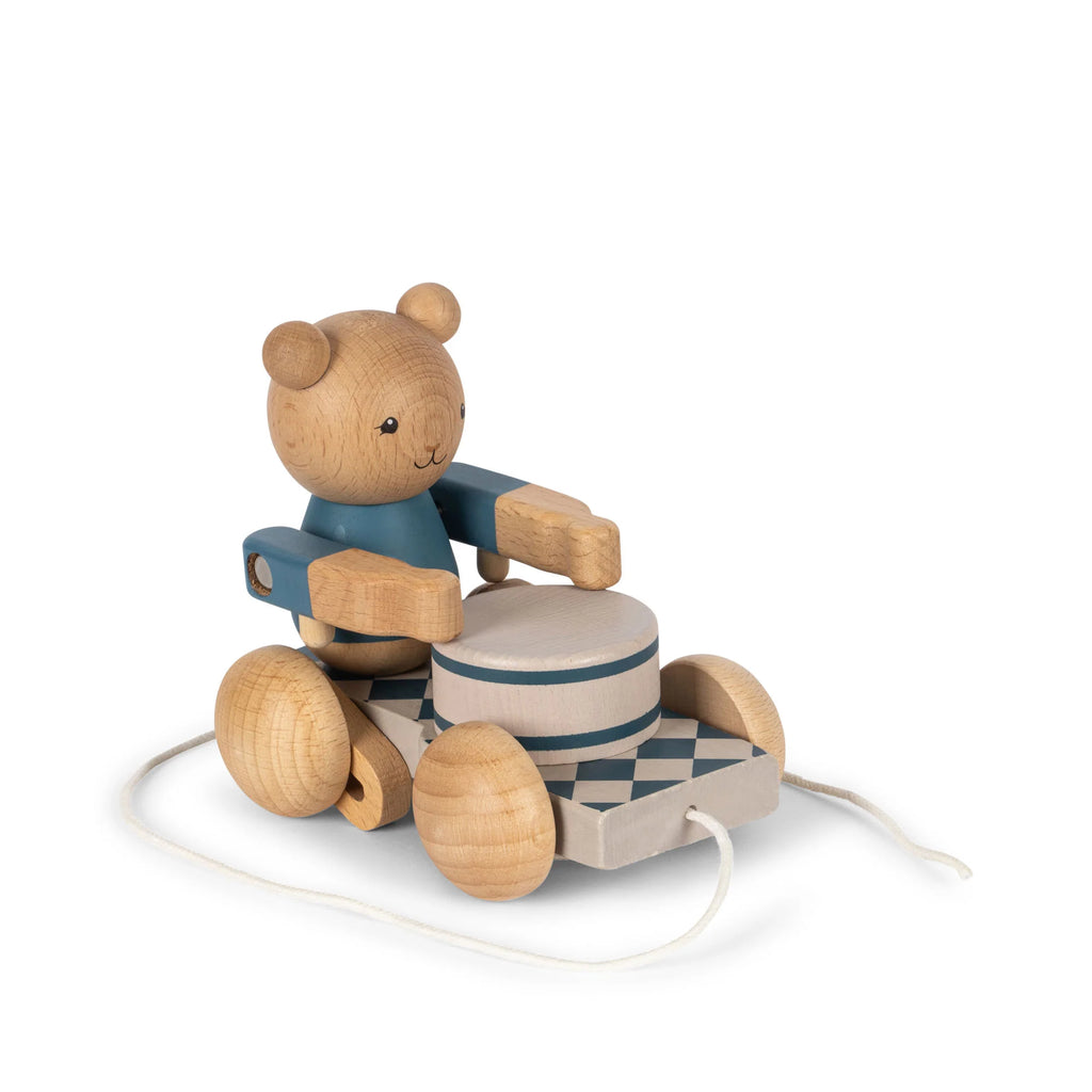 A Wooden Pull Toy - Drummer Bear made of FSC-certified wood, sitting on a small, wheeled cart with striped patterns, isolated against a white background. The bear and cart are connected by a string.