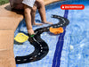 A child sits on the edge of a pool, engaged in imaginative play with the WaytoPlay: Small Flexible Toy Road Set - Ringroad and small boats floating in the water. A red “WATERPROOF” label is prominently displayed in the upper right corner, highlighting that this set is ideal for outdoor adventures.