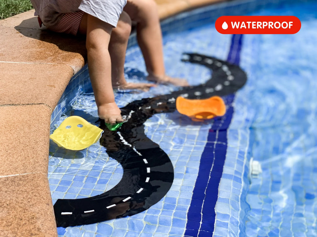 A child sits on the edge of a pool, engaged in imaginative play with the WaytoPlay: Small Flexible Toy Road Set - Ringroad and small boats floating in the water. A red “WATERPROOF” label is prominently displayed in the upper right corner, highlighting that this set is ideal for outdoor adventures.