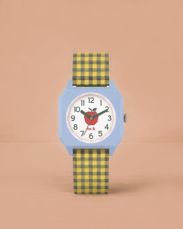 The Sticky Lemon x Mini Kyomo Watch - Apple features a light blue octagonal face, white dial with green numbers, red heart detail, and a yellow-and-black plaid strap—ideal for helping kids learn to tell time. Photographed on a plain peach background.
