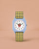 The Sticky Lemon x Mini Kyomo Watch - Apple features a light blue octagonal face, white dial with green numbers, red heart detail, and a yellow-and-black plaid strap—ideal for helping kids learn to tell time. Photographed on a plain peach background.
