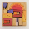 A square wooden tray filled with a Grimm’s Building World - Desert Sand puzzle of geometric blocks in shades of orange, red, yellow, and purple, including two small wooden peg dolls for imaginative free building.