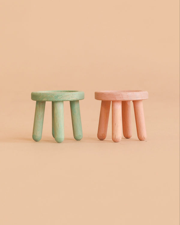 Two small Maileg stools from the Mouse series—one in light rose and the other in light mint—each crafted from beech wood with a vintage paint finish and three round legs, are placed side by side on a beige background.