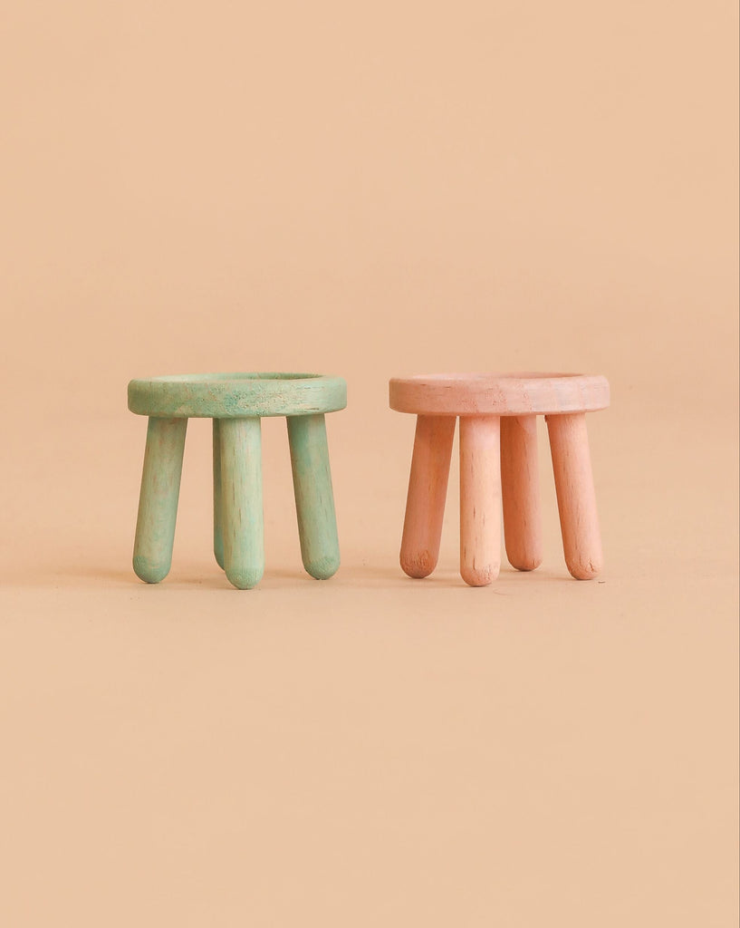 Two small Maileg stools from the Mouse series—one in light rose and the other in light mint—each crafted from beech wood with a vintage paint finish and three round legs, are placed side by side on a beige background.