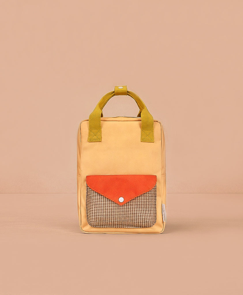 The Sticky Lemon Backpack Small - Envelope - Apple Juice is a small, rectangular yellow backpack with short handles, an orange front pocket flap, checkered pattern beneath the flap, made from recycled PET bags and shown on a plain beige background.