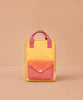 The Sticky Lemon Backpack Medium - Envelope - Apple Grub is a yellow bag with pink handles and a pink snap-button front pocket, made from recycled PET bottles, shown on a beige background.