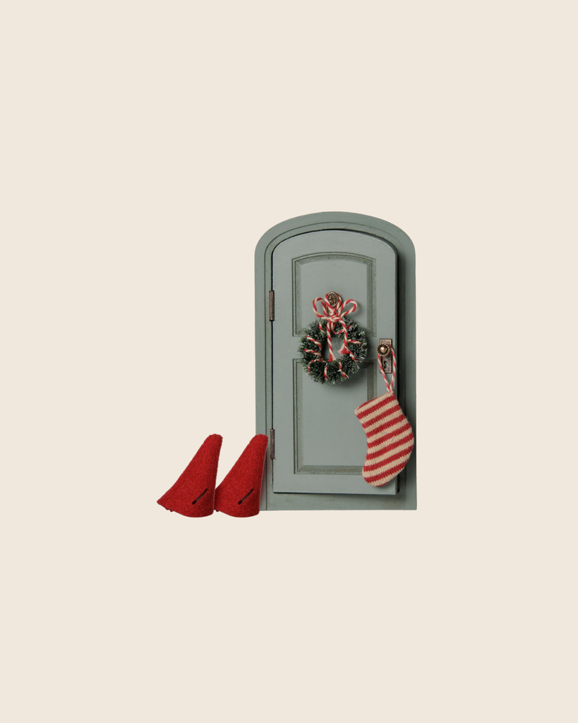 The PRE-ORDER: Maileg Christmas Door Set, Mouse (arriving early November) features a small gray door with a festive wreath and stocking, plus two red elf hats from the Christmas mice set, creating charming holiday decor against a beige background.