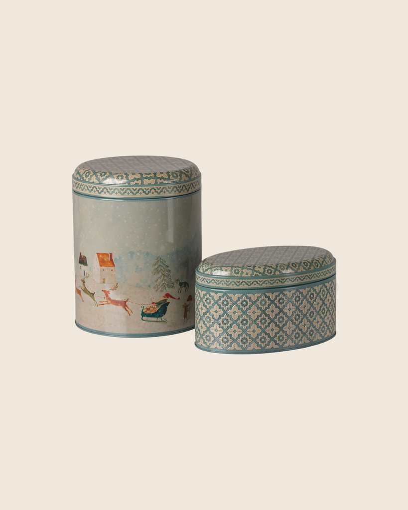 PRE-ORDER: Maileg Metal Box Set - Santa is Coming features two decorative tins on a beige background: a tall, cylindrical Christmas box with a winter scene, and a shorter, oval tin with blue and white geometric patterns. Estimated arrival early October.