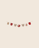 The PRE-ORDER: Maileg Christmas Garland features fabric ornaments—bells, mittens, and a heart—in red, beige, and white patterns on a string, ideal for cozy holiday décor. Estimated arrival mid October.