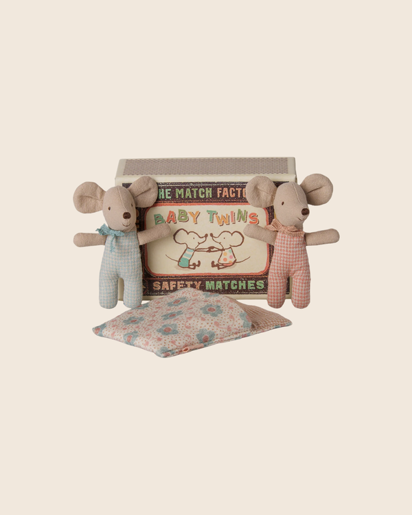 Two small PMaileg Twins, Baby Mice in Matchbox - Checker are dressed in pastel rompers and posed in front of their vintage-style matchbox bed labeled “Baby Twins,” with a patterned pillow placed beside them on a plain beige background.