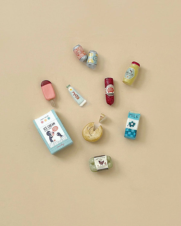 The Maileg Miniature Grocery Box offers a charming collection of mini food items like an ice cream cone, carton, and popsicle. Perfect for Maileg food set fans or pretend play, these artful toy foods are lively displayed on a beige background.