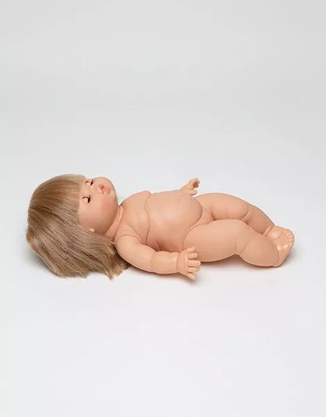 A Minikane Baby Doll With Sleeping Eyes (13") - Yzé, featuring beige skin and short brown hair, lies on its back with a natural vanilla scent against a plain white background.