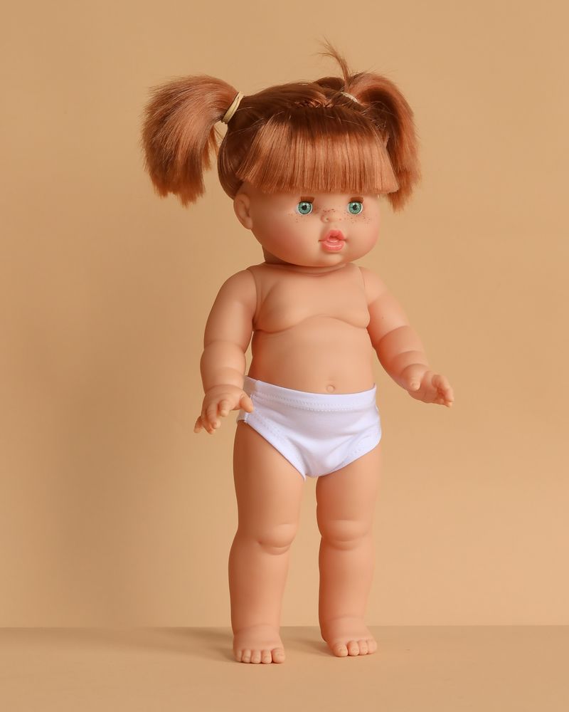 The Minikane Standing Doll (14") - Gabriella features light skin, green eyes, and brown pigtails. This anatomically correct, made-in-Spain doll comes wearing white underwear; clothing is sold separately. Stands against a beige background.