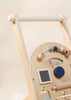 The Wooden Activity Walker features a white handle, colorful beads, spinning gears, a small chalkboard, and simple illustrations on the front panel—making it perfect for little ones discovering sensory toys. Set against a neutral background.