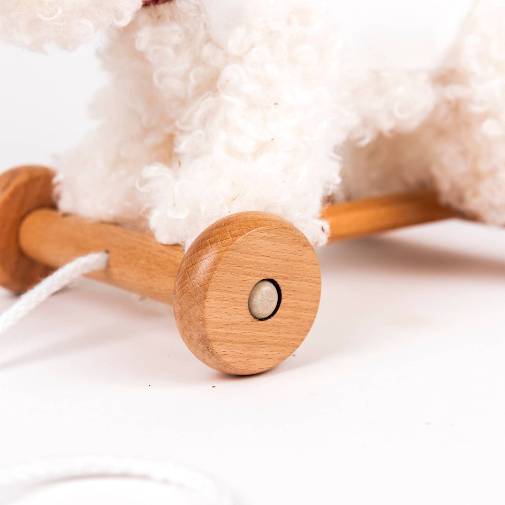 Close-up of Pull-Along Lola: a fluffy white toy on a light brown wooden base with wheels and a white pull string, making it ideal for developmental play or as a delightful toddler gift.