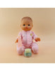 A baby doll in a pink onesie sits against a beige background, clutching a small pink bottle. In front of it is a jar labeled "Tiny Tummies - Apple jelly food" by Tiny Harlow, offering the promise of mealtime magic with every spoonful.