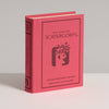 A red hardcover "Board Game: Scattergories Vintage Bookshelf Edition" stands upright on a white surface, featuring a stylized head and playful symbols on its cover, inspired by the original 1988 edition.