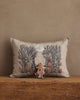 The Coral & Tusk Spooky Forest Pocket Pillow with a forest and pumpkin design rests against a beige wall, while a small pumpkin-themed doll sits in front on the wooden surface.