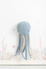 A soft blue Octopus Stuffed Animal hangs on a white Deco Wall decorated with subtle undersea illustrations featuring coral and bubbles, ideal for a children's room decoration.