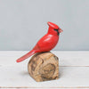 The Hand Carved Ornament - Cardinal Bird - Male - 7"H features a vivid red cardinal with a black face mask perched on natural wood, making it a charming anniversary gift against a light gray background.