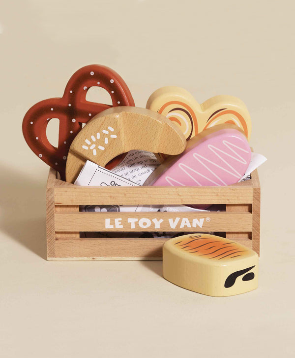 The Bakery & Patisserie Wooden Market Crate includes eco-friendly toy pastries—a pretzel, croissant, heart cookie, and pink frosted treat—with a butter pretend play toy placed in front.