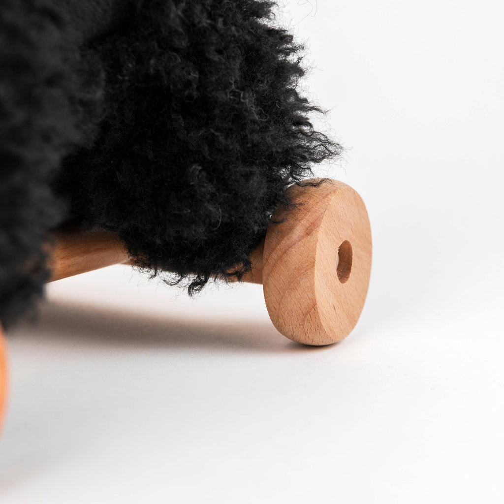 Close-up of Pull-Along Walter's wooden wheels, attached to the toy which is covered in thick, curly black fabric, set against a plain white background.