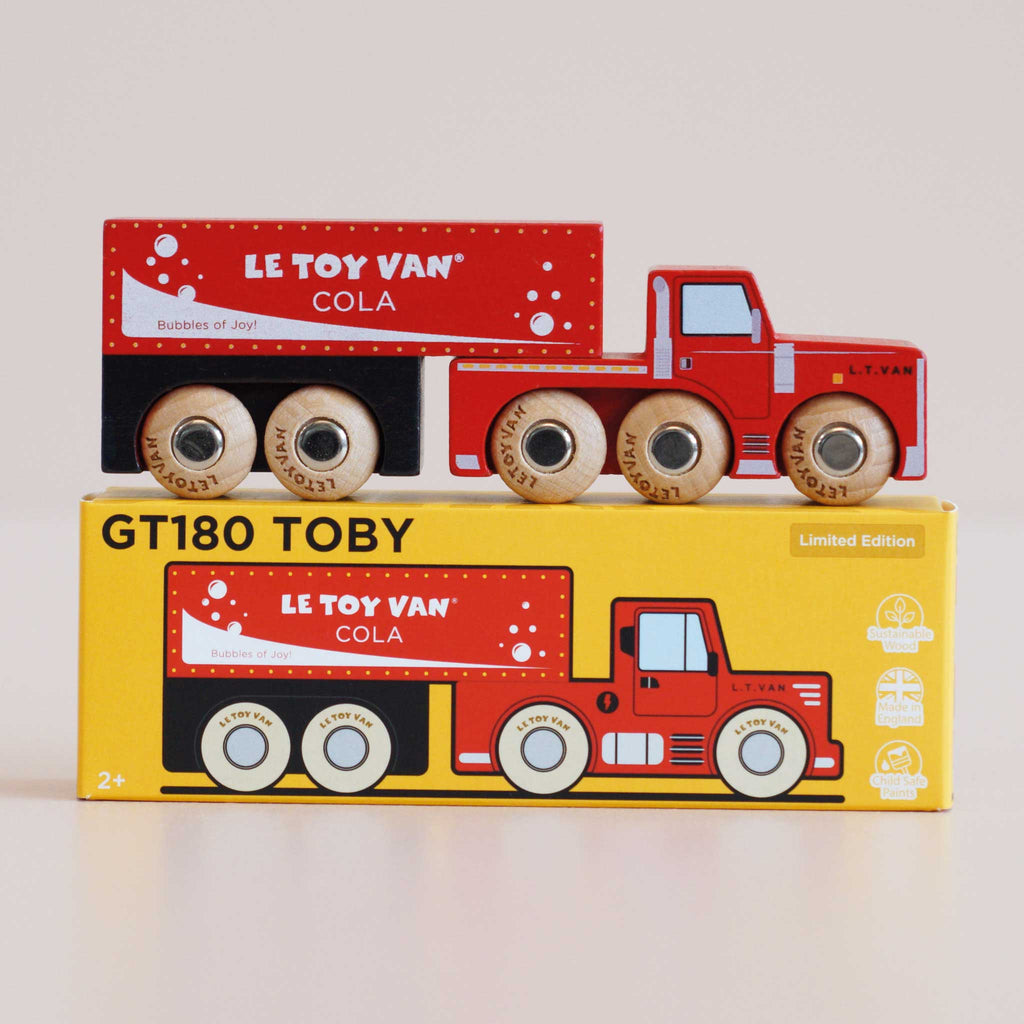 Drawing inspiration from vintage delivery vehicles, the No. 33 GT180 Toby | Made in England wooden cola truck and trailer rest atop a yellow box marked “GT180 TOBY Limited Edition.” The red collectible toys, adorned with “Le Toy Van Cola” branding, spark imaginative storytelling for both children and collectors.
