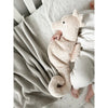 A baby cuddles the Senger Naturwelt Cuddly Animal - Seahorse while lying in a crib, dressed in white with a textured gray blanket nearby on a light-patterned bedsheet.