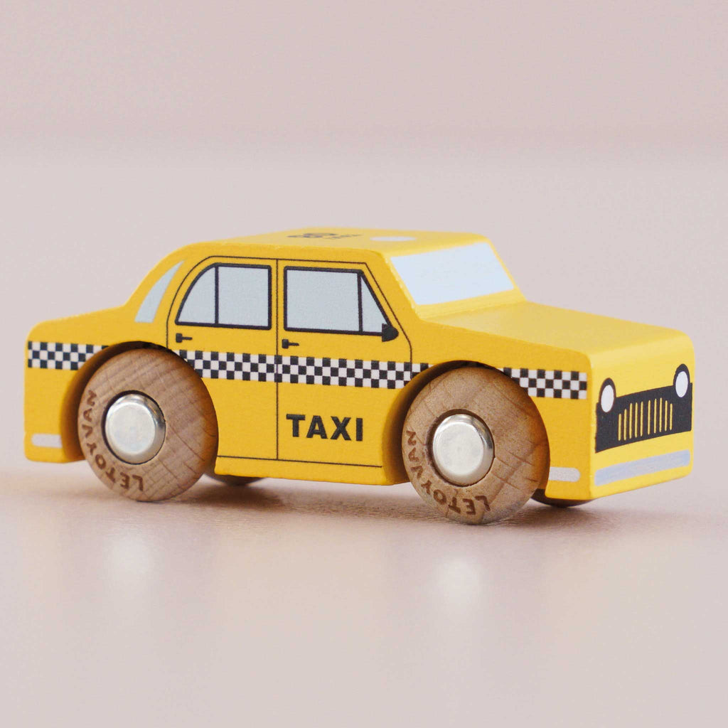 A No. 39 GT245 Trixie, made in England, sits on a light surface—a yellow wooden taxi adorned with black checkered stripes and sturdy wheels—ready to inspire imaginative play as a charming New York cab.