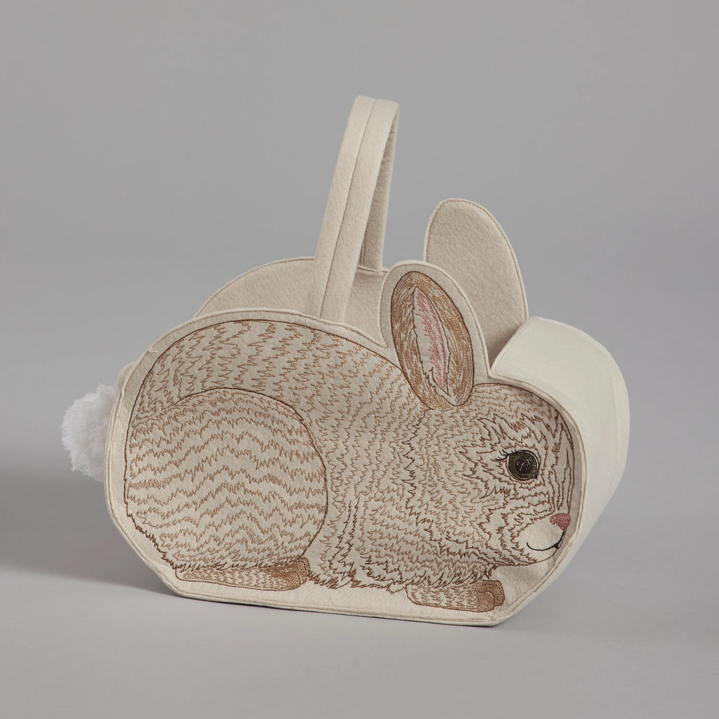 A Coral & Tusk Bunny Basket, a rabbit-shaped children's bag with a brown and white color scheme, featured in a profile view with an embroidered bunny and a fluffy white tail detail, against a plain gray background.