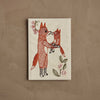 The Coral & Tusk Fox Mama Card features embroidered art of an adult fox hugging a smaller fox, surrounded by pink flowers and green leaves on beige fabric—perfect as a heartfelt new parent gift or charming keepsake.