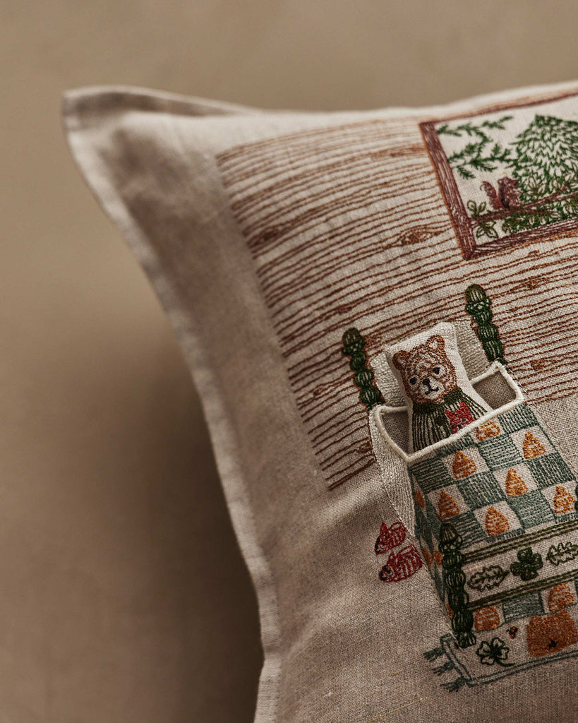 A close-up of the Coral & Tusk Three Little Bears Pocket Pillow, featuring embroidered bears tucked in bed, a tree outside their window, and cozy details in earthy tones—a charming pillow inspired by Goldilocks and the Three Bears. Ships in one week.